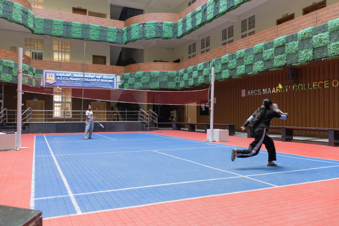 Students playing badminton on the indoor campus sports court at AECS Maaruti College of Nursing